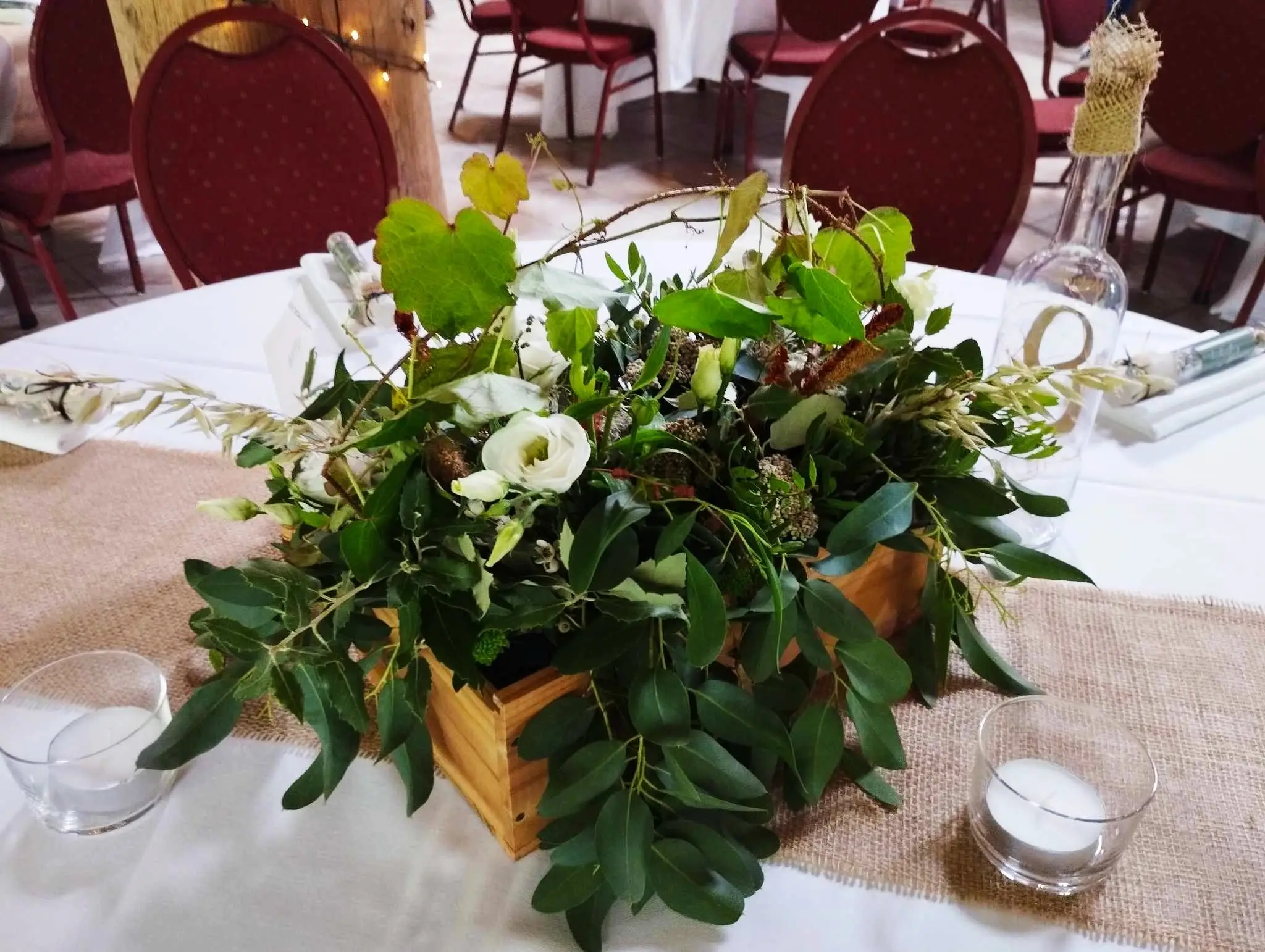 Centre de table en caisse de bois : eucalyptus, fleurs blanches et photophores.