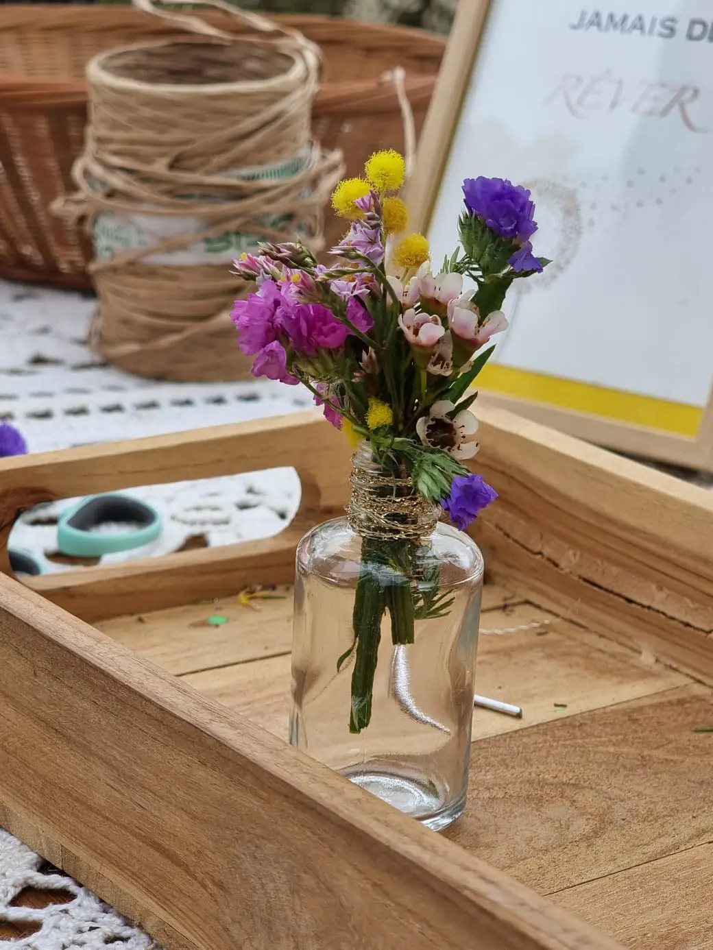 Petit bouquet de mimosa et de statice dans une fiole, posé dans un plateau en bois.