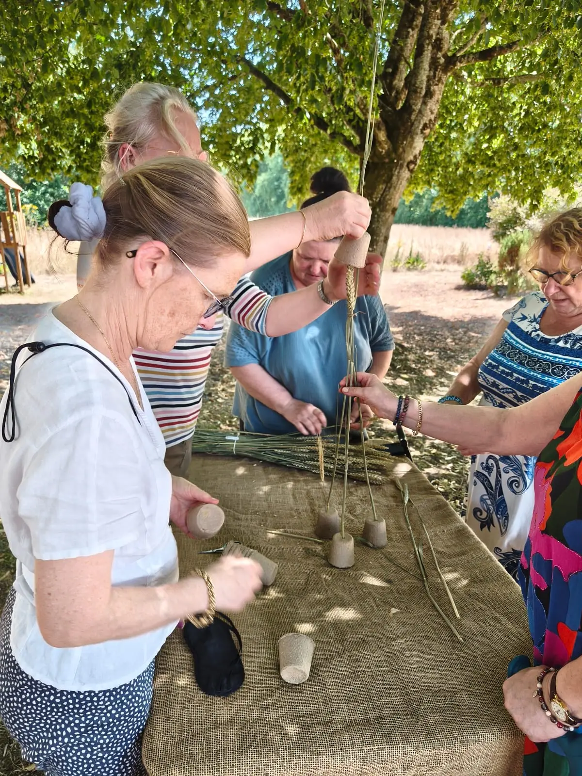 Des mains assemblent graminées et petits pots autour de la table.