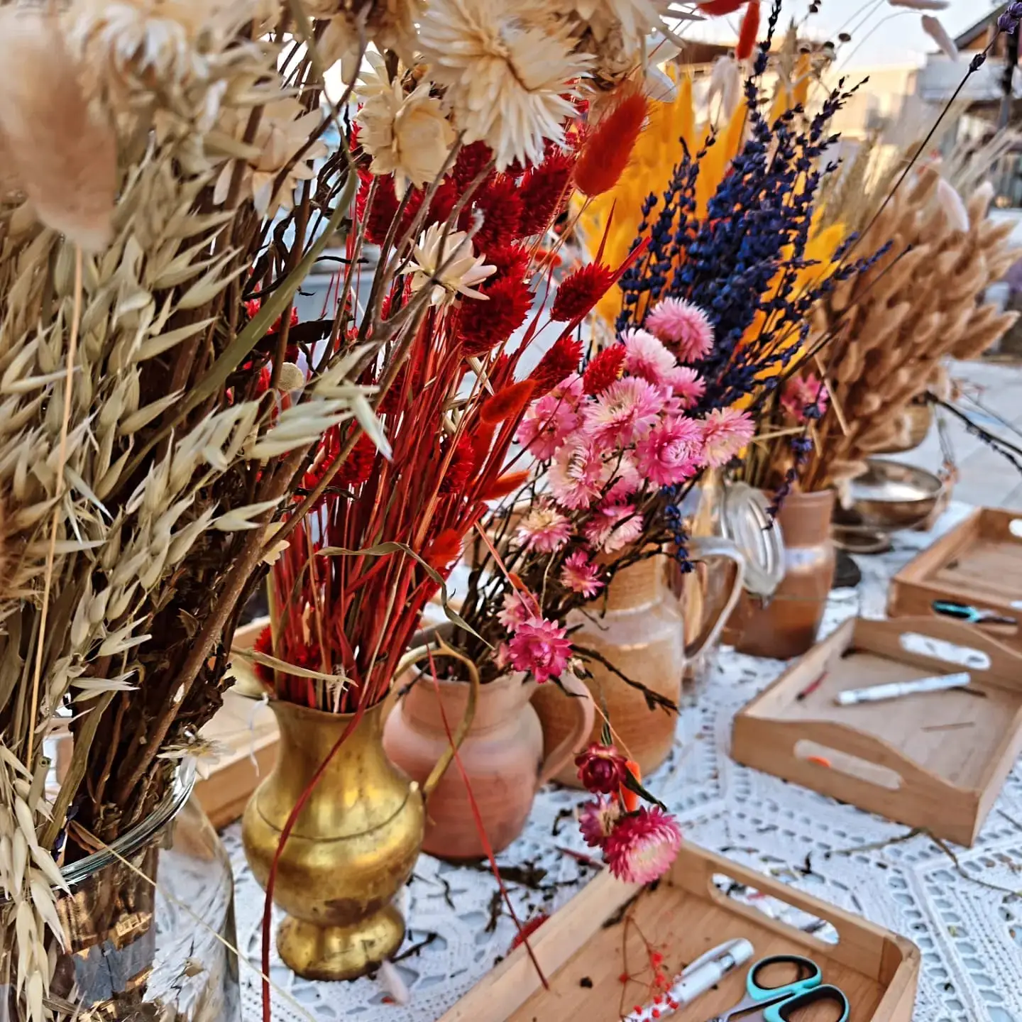 Fleurs séchées, vase en laiton et plateaux d’outils prêts pour l’atelier.