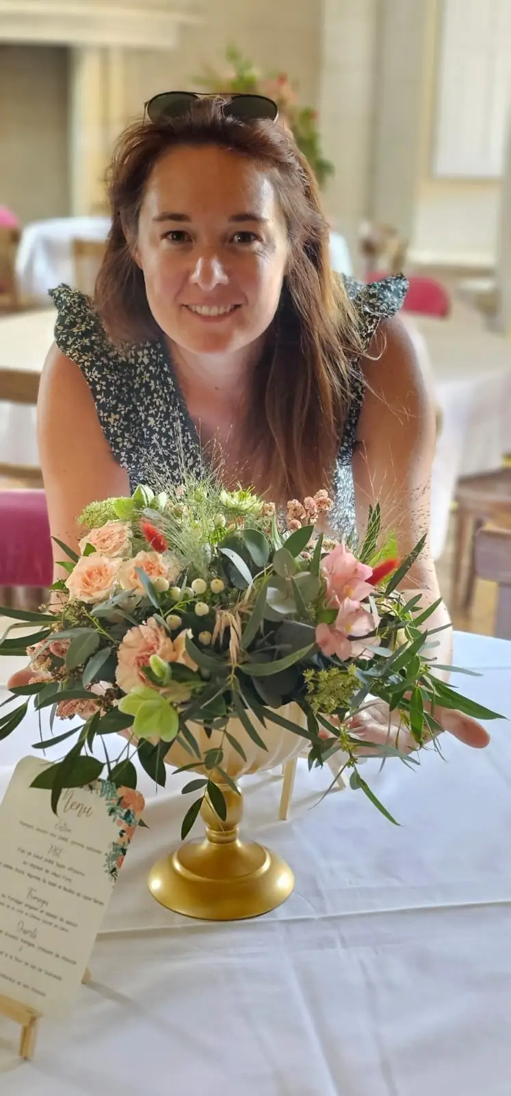Laurie Delannoy sourit derrière un centre de table fleuri qu’elle vient de composer.