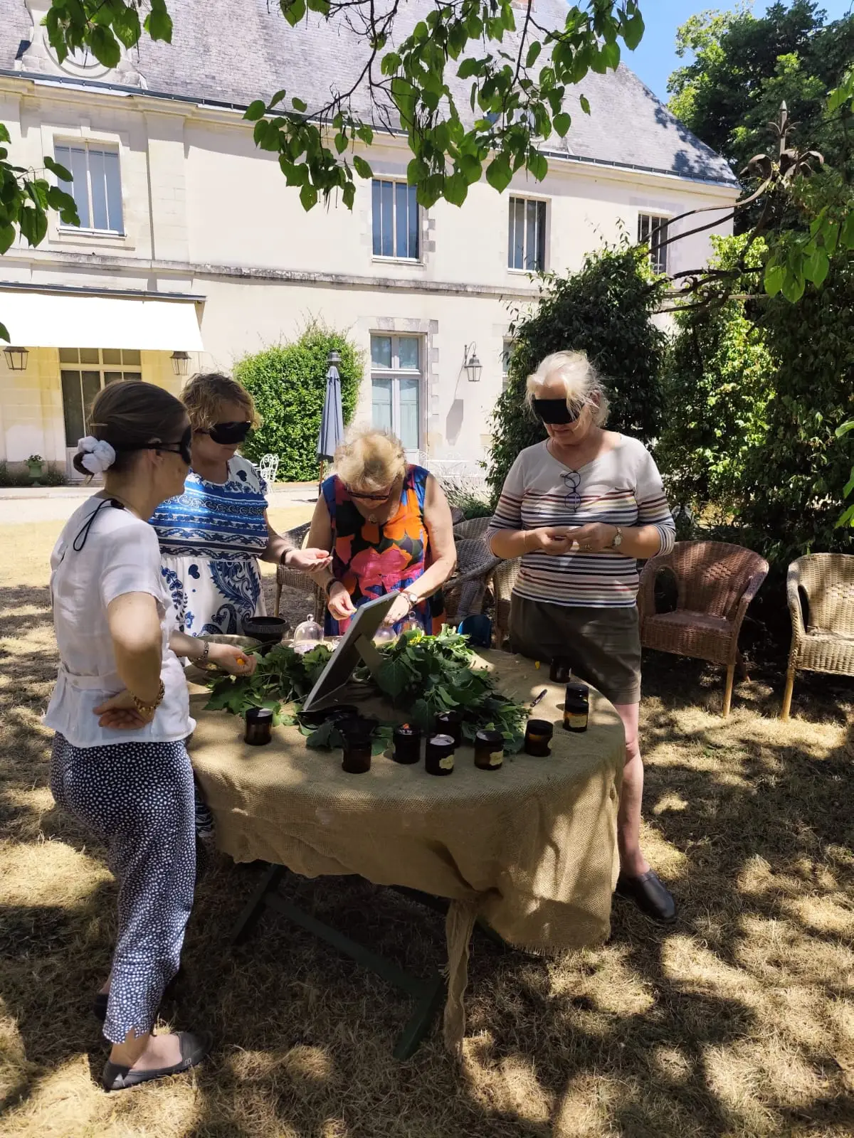 Les yeux bandés, des participantes reconnaissent des plantes à l’odeur autour d’une table en plein air.